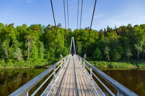 Cable-stayed wooden path bridge over Gauja river with forest at the background Stock Photos