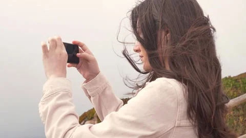 Cabo da roca in portugal. cloudy windy day. girl makes selfie on a smartphone.  Stock Footage 157931607