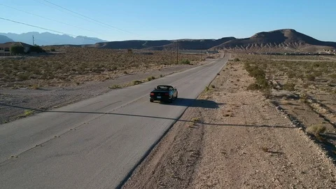 Cabrio driving through desert road - drone following Stock Footage 107879534