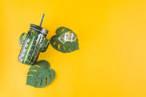 Cactus shape jar with ice cubes artificial monstera leaves yellow background Stock Photos