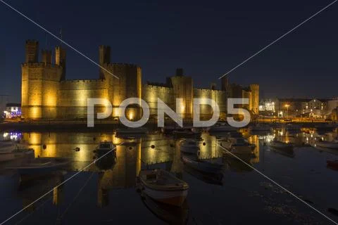 Caernarfon castle and harbour with boats and reflections at night Stock Photos