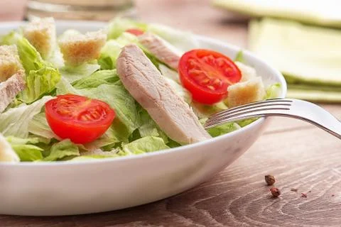 Caesar salad with chicken on a light natural table with cutlery. Stock Photos