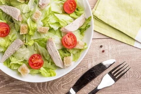 Caesar salad with chicken on a light natural table with cutlery. Stock Photos