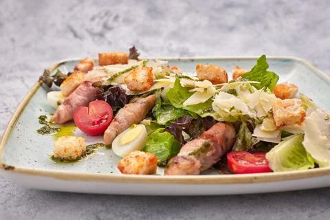 Caesar salad with herbs chicken bacon eggs and tomatoes on a square light pla Stock Photos