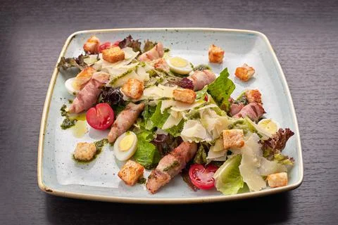 Caesar salad with herbs chicken bacon eggs and tomatoes on a square light pla Stock Photos