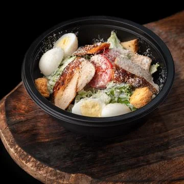 Caesar salad in round black lunchbox Stock Photos