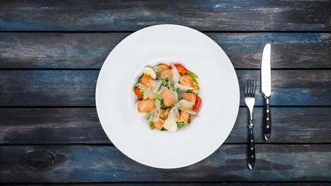 Caesar salad with salmon rotating on a plate. Served with cutlery on a colored Stock Footage 129185474