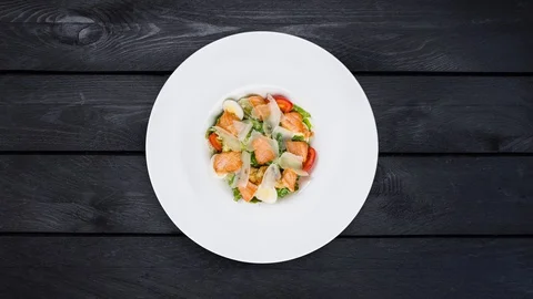 Caesar salad with salmon rotating on a plate. Is at a black wooden background Stock Footage 129185705