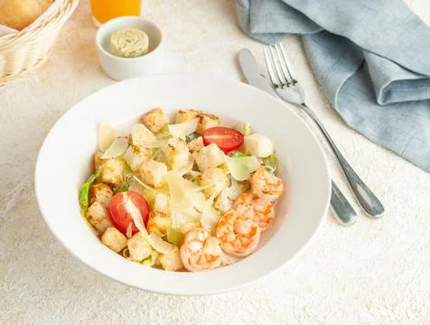 Caesar salad with shrimps. On a white plate. Nearby are cutlery and a blue na Stock Photos