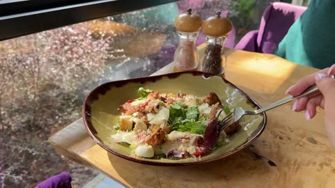 Caesar salad on a sunlit wooden table near the window with salt and pepper Stock Footage 319780485