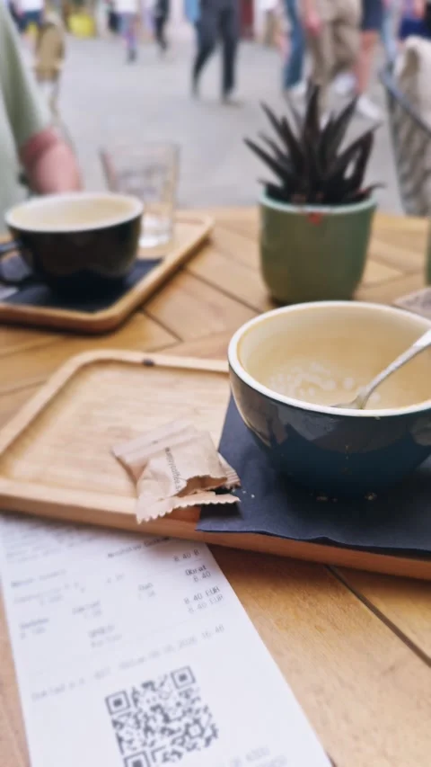 A café receipt and empty coffee cups rest on an outdoor table as visitors walk Stock Footage 341112923