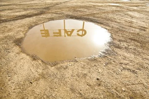 Cafe sign reflection in puddle of water on the ground in the dirt. Stock Photos