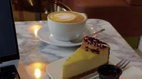 Cafe table with latte and cheesecake beside laptop edge in warm upscale light Stock Footage 344966512