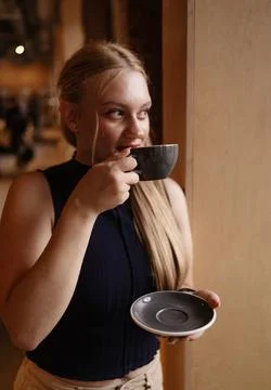 Cafe visitor drinks coffee alone. Beautiful blonde girl whiles away time Stock Photos