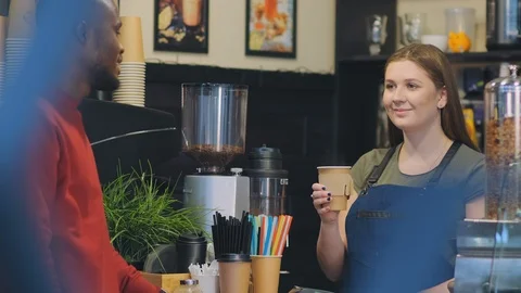 Cafe worker gives coffee in cup to client with dark skin 스톡 동영상 125553533