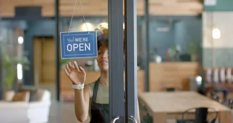 Cafe worker is reaching up, flipping closed sign to open and pulling door to Stock Footage 336437686