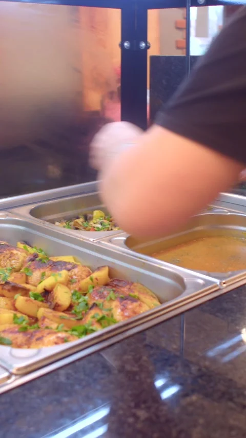 Cafeteria server reaching to serve roasted potatoes and gravy from stainless 库存影片 336534371