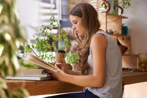Caffeine-boosted studying in progress...a young woman reading a book in a coffee Foto stock