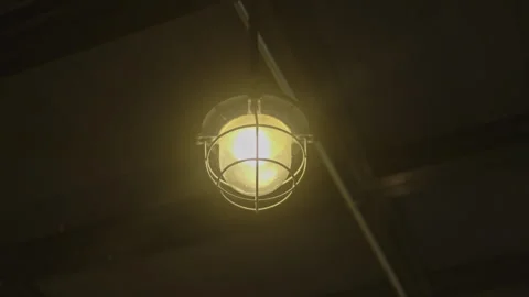 Caged industrial ceiling light glowing in a dark interior Video stock 347035724