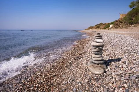 A cairn made out of flat rocks erected with balance at the water's edge next Stock Photos