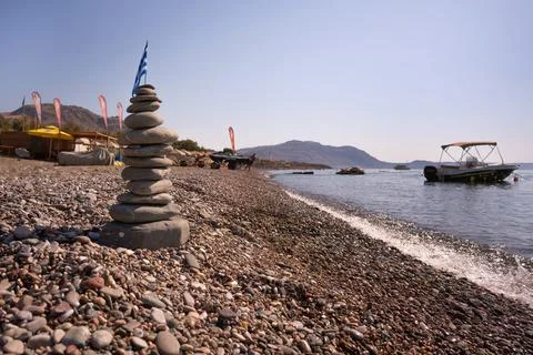 A cairn made out of flat rocks with a flag on top, on a sunny pebble beach .. Foto stock
