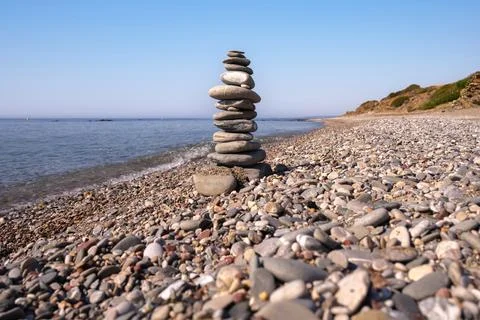 A cairn made out of flat rounded rocks erected on a sunny pebble beach near.. Stock Photos