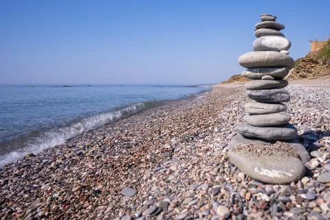 A cairn made out of flat rounded rocks erected on a sunny pebble beach near.. Stock Photos