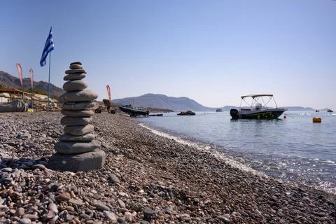 A cairn made out of flat rounded rocks erected on a sunny pebble beach with f Stock Photos