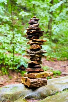 Cairn stack of small stones against bright green woods Stock-Fotos