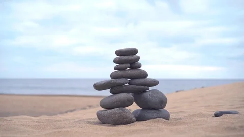 The cairn stands on the sand. The hand adds the last stone to finish the cairn Stock Footage 101754322
