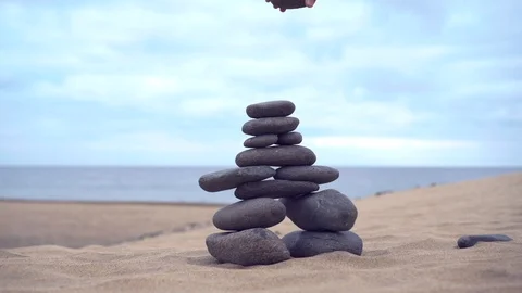 The cairn stands on the sand. The hand adds the last stone to finish the cairn Stock Footage 101754453