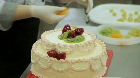 Cake decorating. Close up of baker hands decorate big cream cake with fruits Stock Footage 50475716