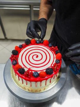Cake designer decorating a chocolate drip cake with berries and gold on the top Stock Photos