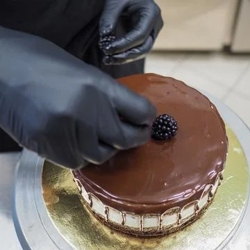 Cake designer decorating a chocolate drip cake with berries and gold on the top Stock Photos