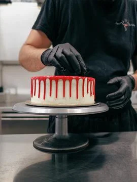 Cake designer decorating a red drip cake with berries on the top Stock Photos