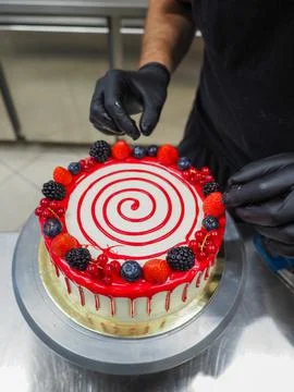 Cake designer decorating a red drip cake with berries on the top Stock Photos