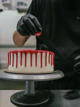 Cake designer decorating a red drip cake with berries on the top Stock Photos