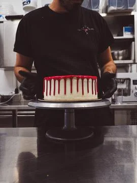 Cake designer decorating a red drip cake with berries on the top Stock Photos