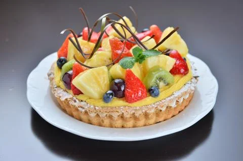 Cake of fruit with strawberry pineapple grape kiwi on white plate in restaura Stock Photos