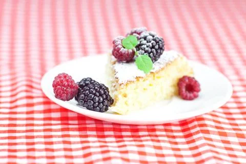 Cake with icing, raspberry, blackberry and mint on a plate on plaid fabric Stock Photos