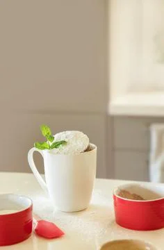 Cake in a mug in white cup, baking ingredients on white kitchen table, baking at Stock Photos