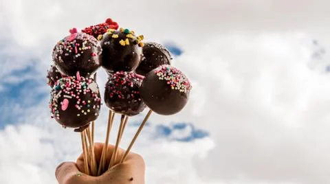 Cake pops in a hand in front of the cloudy sky Stock Photos