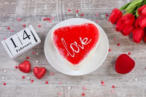 Cake in the shape of a heart, red tulips, gift box and wooden block calendar Foto stock