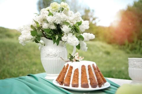 Cake with some cups on picnic table decorated with flowers, candles, vase in Stock Photos