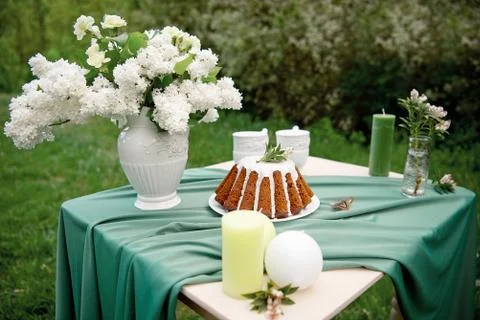 Cake with some cups on picnic table decorated with flowers, candles, vase in Stock Photos