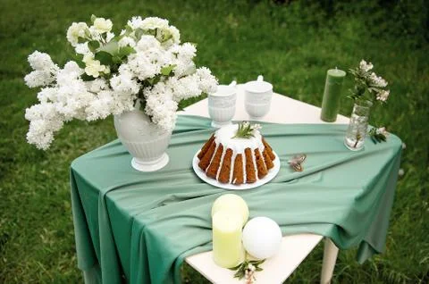Cake with some cups on picnic table decorated with flowers, candles, vase in Stock Photos