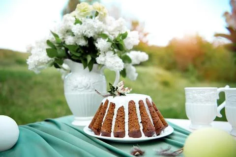 Cake with some cups on picnic table decorated with flowers, candles, vase in Stock Photos