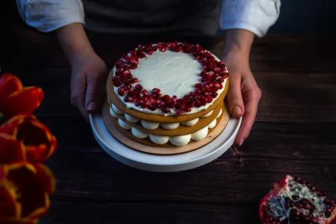 The cake stands on a white stand, decorated with cream and pomegranate on top Stock Photos