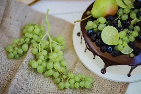 Cake under the chocolate icing, decorated with pear, grapes and lime. Stock Photos