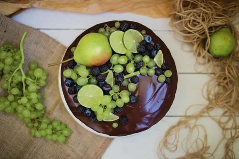 Cake under the chocolate icing, decorated with pear, grapes and lime. Stock Photos